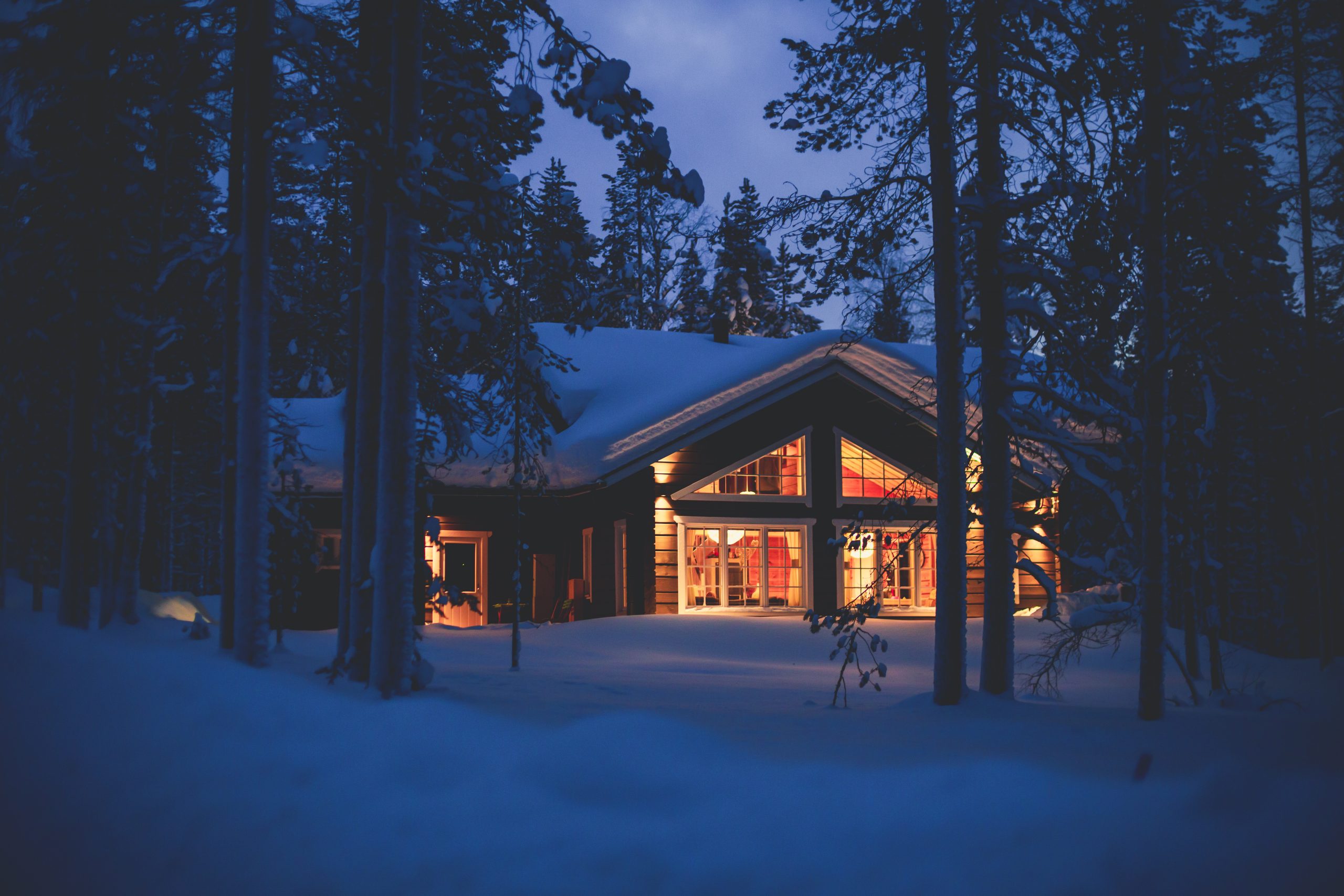 A cozy wooden cabin cottage chalet house covered in snow near ski resort in winter with the lights turn on VINTERFERIE Kampanje -20%